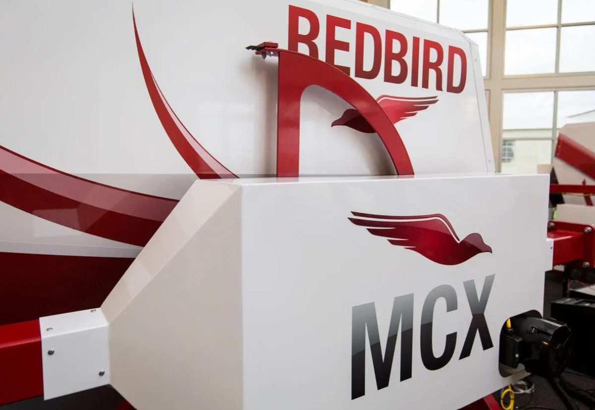 The Redbird MCX cockpit mounted on its red full-motion actuator frame in the hangar
