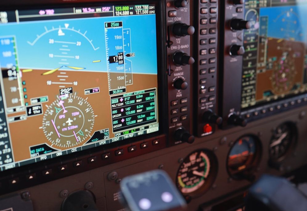 A glass cockpit instrument panel with a hand on the yoke